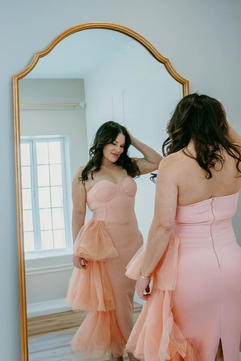 Woman in a pink strapless dress posing in front of a large gold trimmed mirror