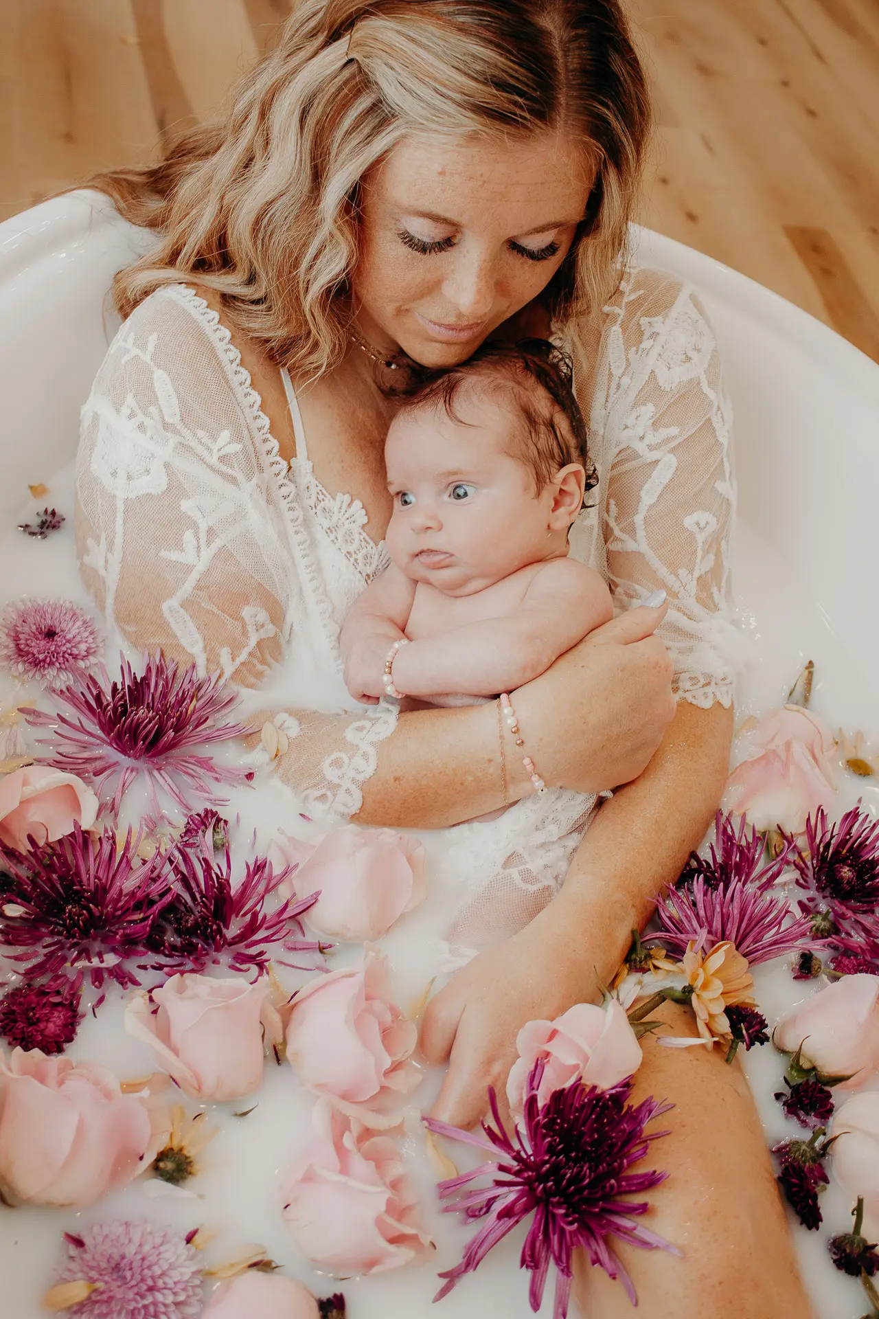 Mother clutching her baby in a milk bath full of flowers
