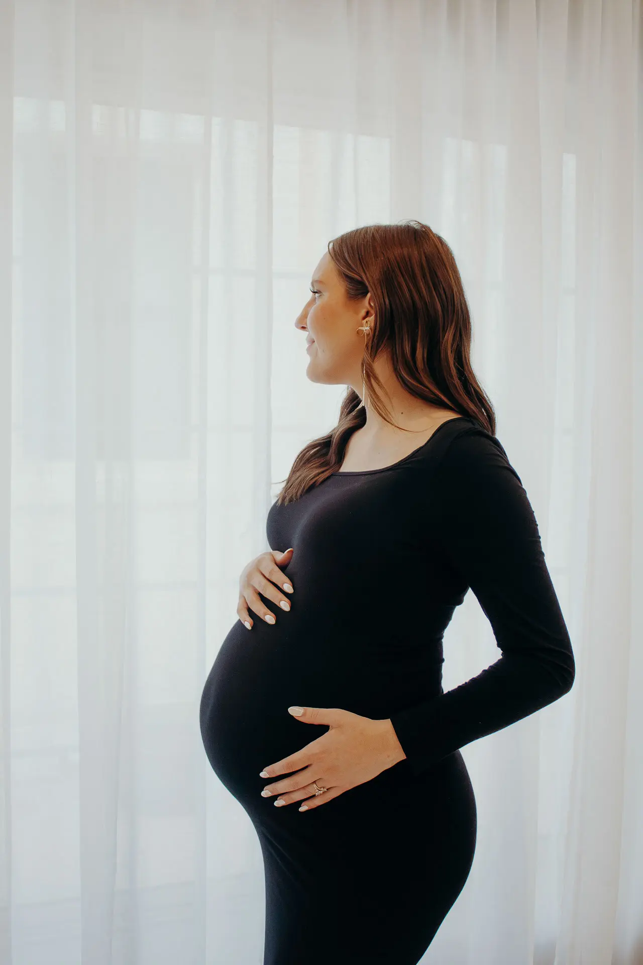 Pregnant woman with her hands on her baby bump looking outside