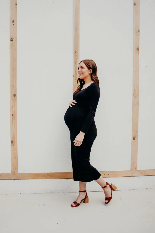 Pregnant woman posing sideways in front of a wood trimmed wall